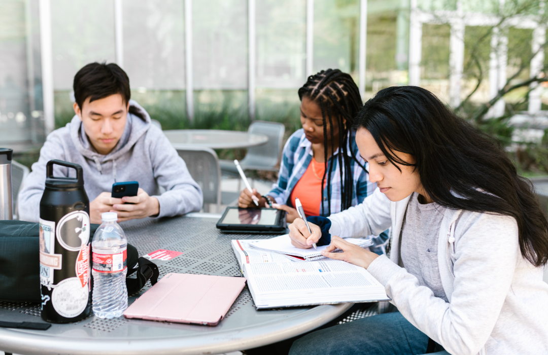 A group of college students studying at an outdoor table.