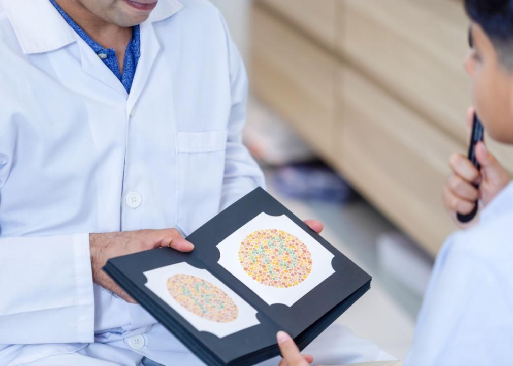 A close-up of a doctor showing a book with two colorful circles on a black-and-white background to a young male patient in front of him.