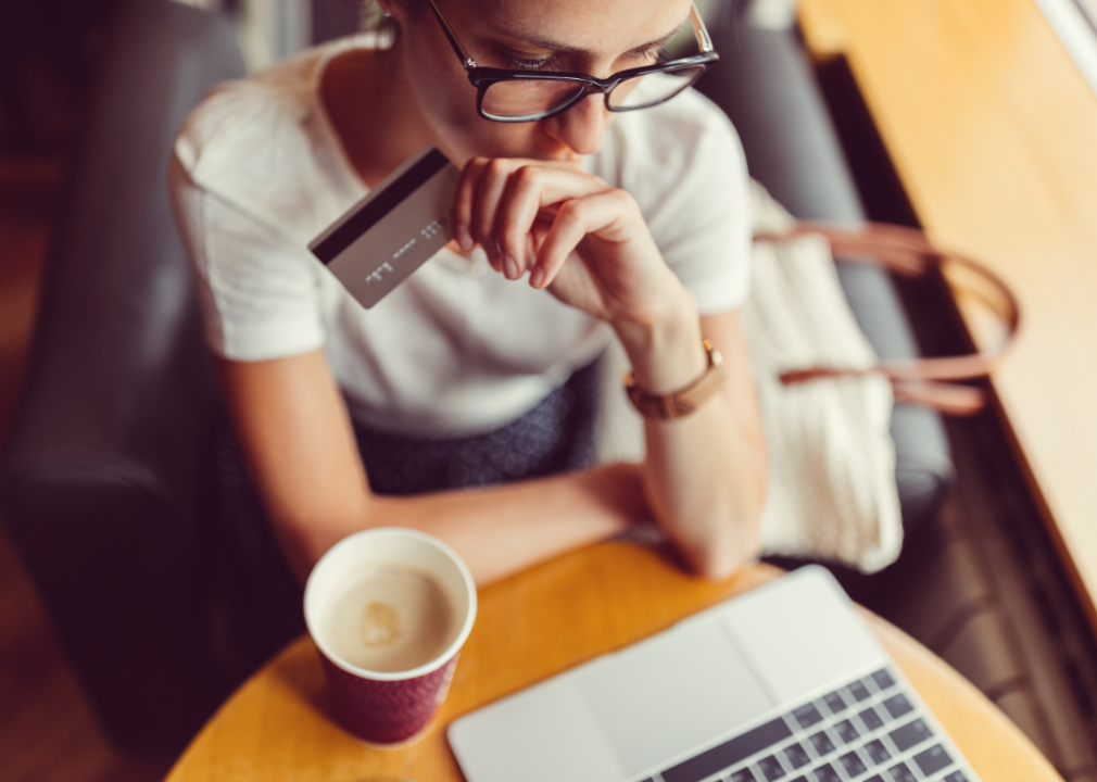 A thoughtful young woman holds a credit card and studies at her laptop