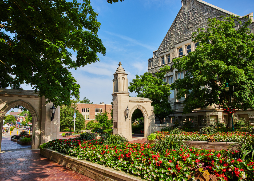 A summer garden in front of stone gates and buildings at Indiana University.