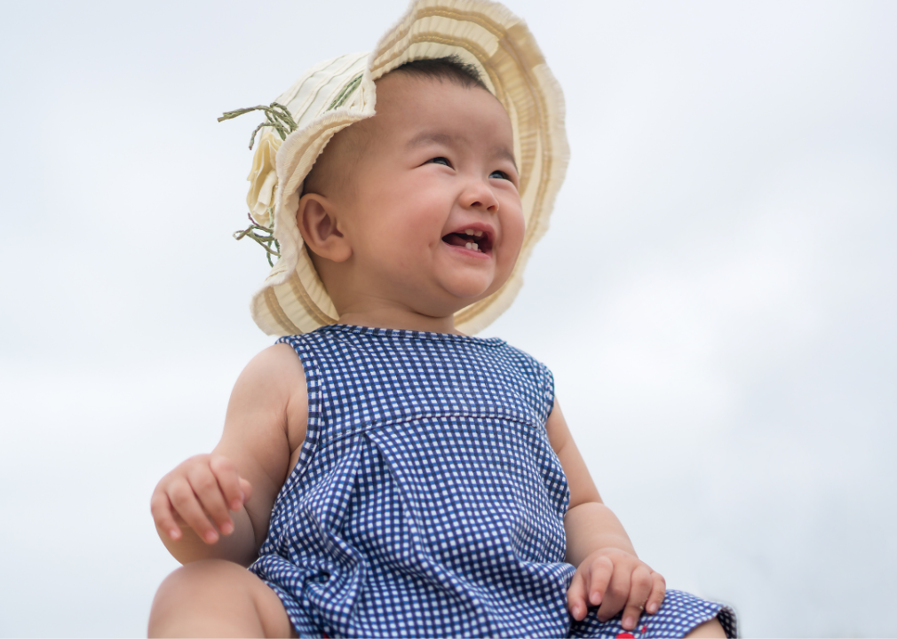 Asian baby girl smiling in summer dress and hat.