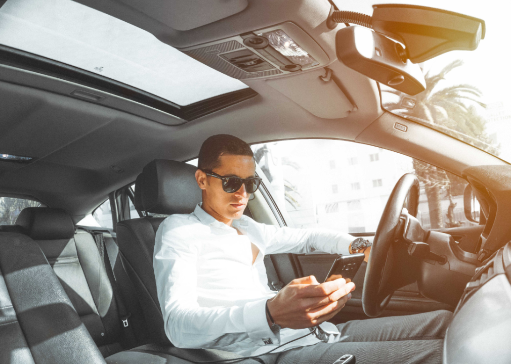 A man in a white dress shirt in a car looking at a cell phone.