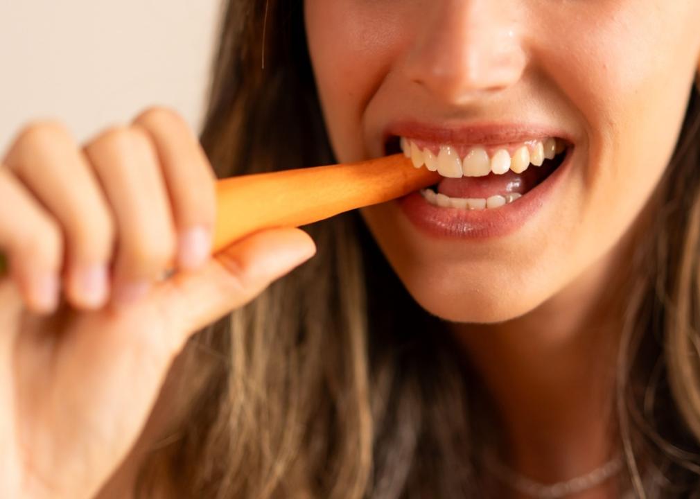 Close-up of a young woman with a carrot in her mouth.