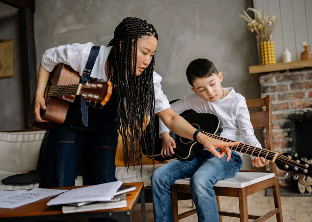 A female music teacher showing a student cords on a guitar.