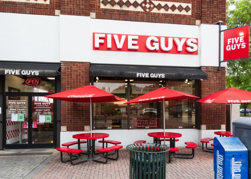 A Five Guys with red umbrellas and tables out front.