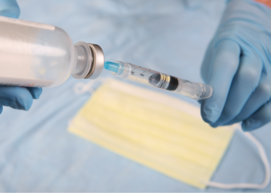 Gloved hands fill a syringe with vaccine