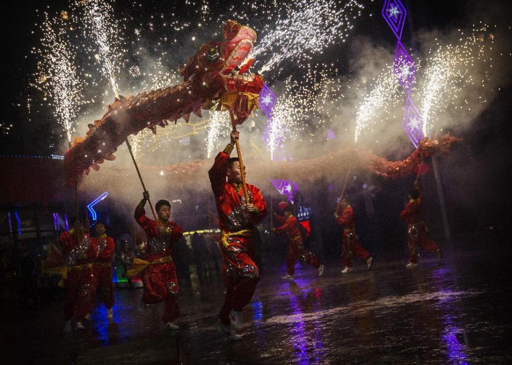 Performers dance in the street holding dragon lanterns with fireworks coming out of it. 