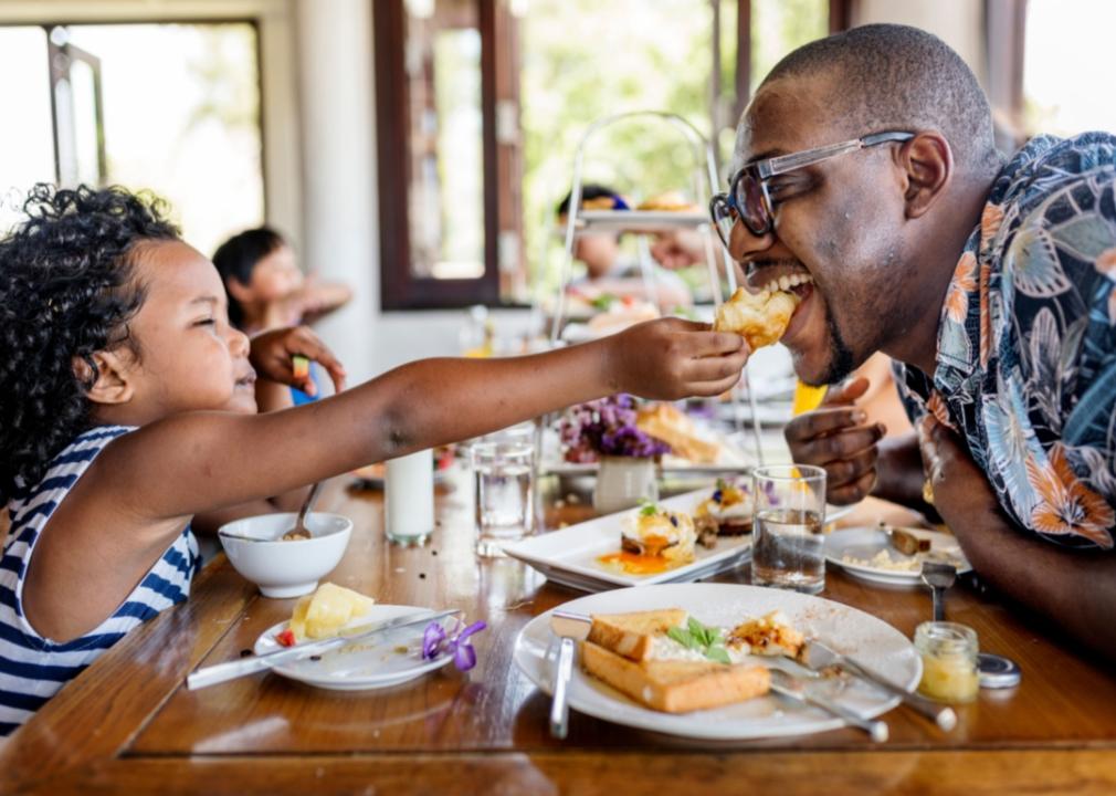 A young African-American girl tenderly gives her father a piece of food at a restaurant.