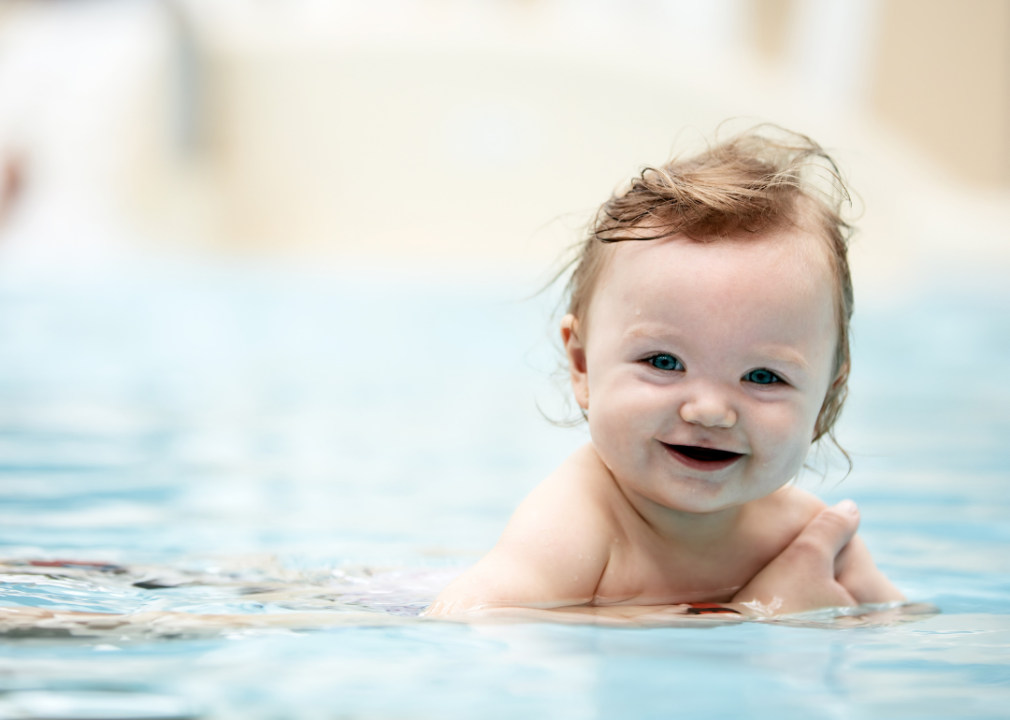 A baby girl in a pool smiling.