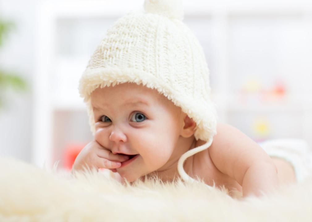 A baby girl looking into the camera wearing a white hat.