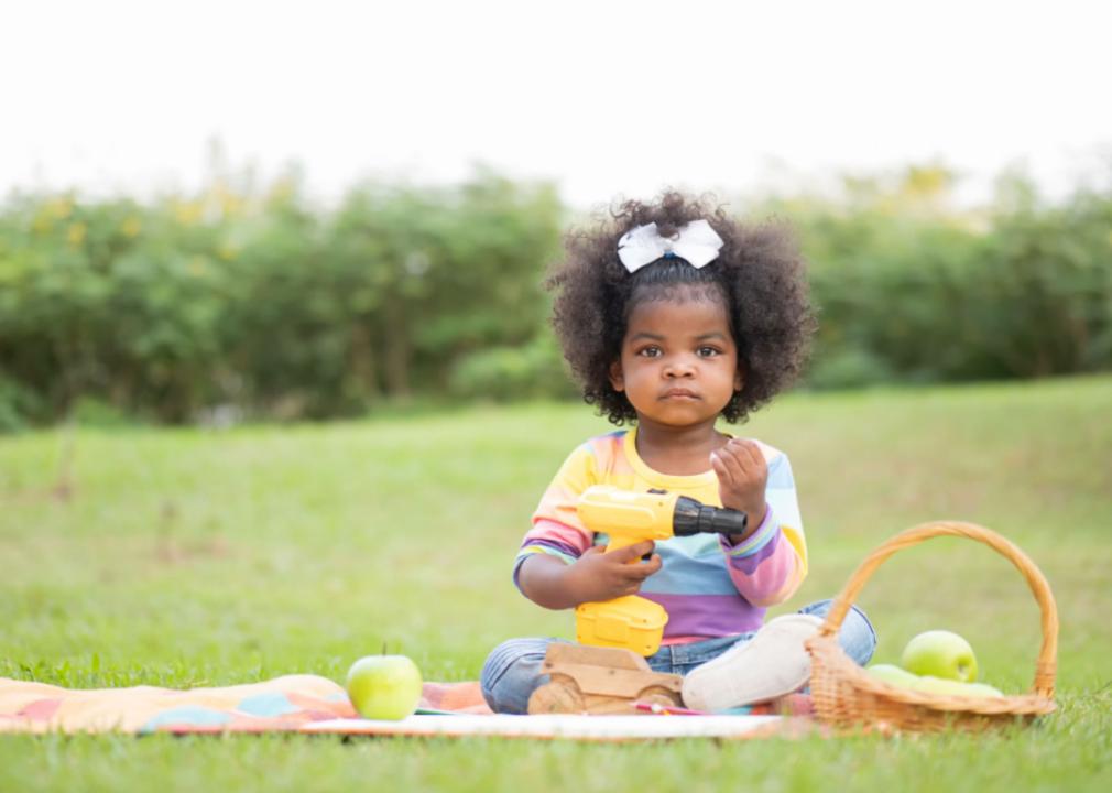 African American girl playing outdoors holding a toy drill. 