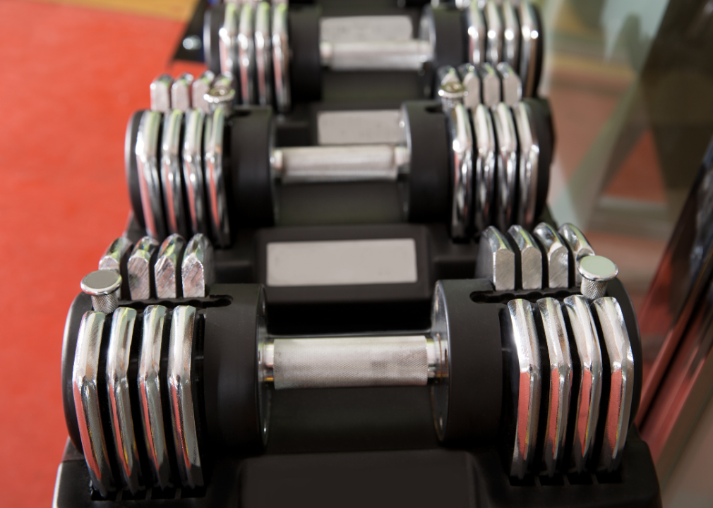 Adjustable dumbbells on a rack in front of a red floor.