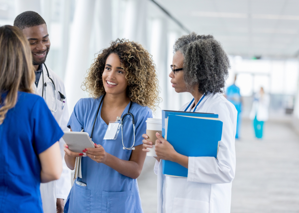 A group of medical staff, three women and a man standing close.  A young woman holding a flat device in her hands looking at the woman in front of her.  