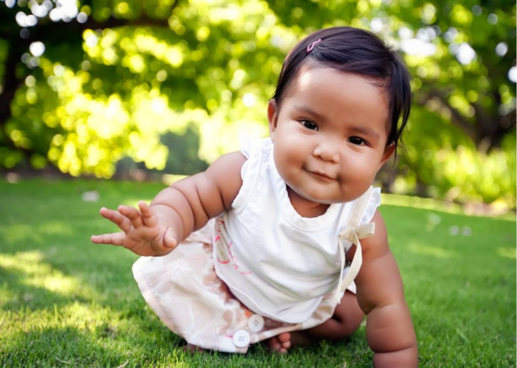 Hispanic baby girl with a smile on her face, reaching out to take her first crawling step.