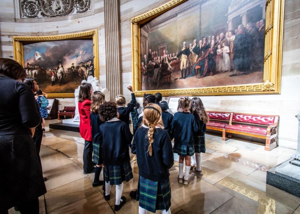 A group of kids wearing headphones looking at large historical paintings hanging on the walls.