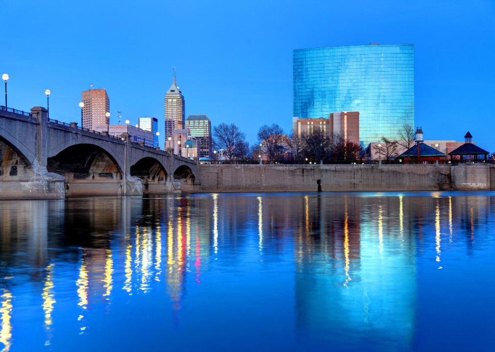 A city skyline across a blue, calm river. The most prominent feature is a long concrete bridge spanning the river. 