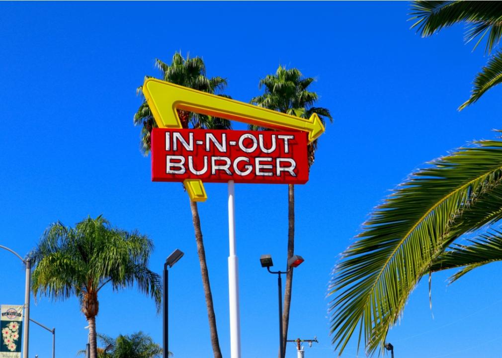 In-N-Out Burger restaurant sign against a vibrant blue sky and palm trees.