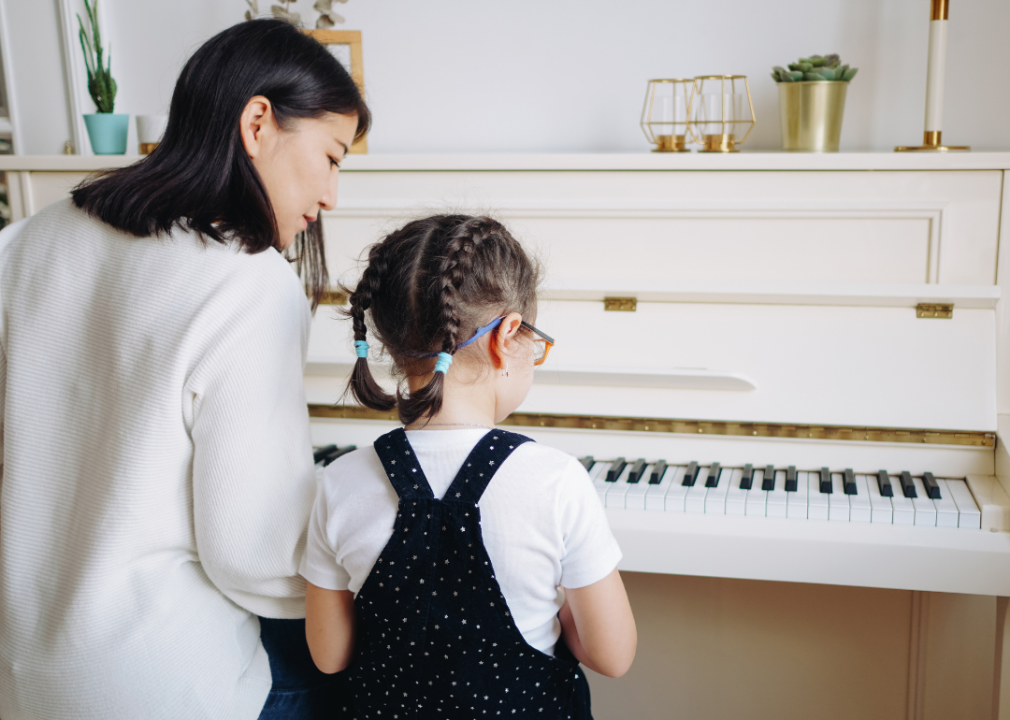A woman and a little girl sit at a piano.
