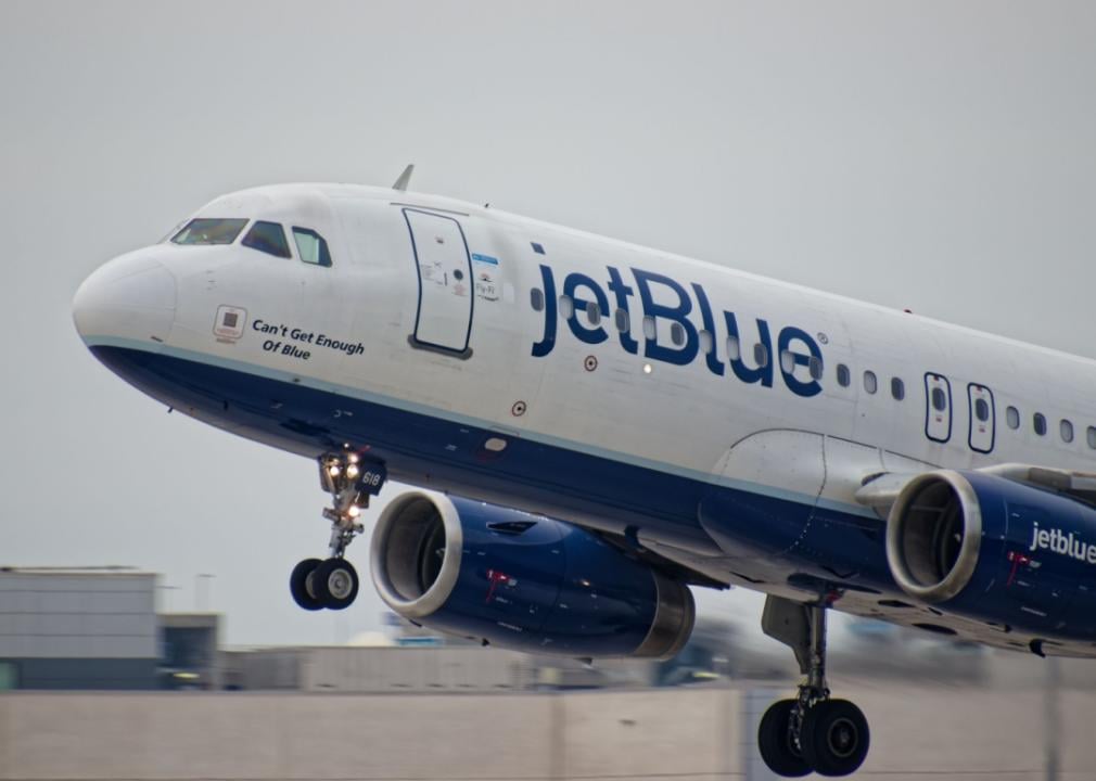 Close up of the front, white plane with a blue stripe running along its fuselage. The JetBlue logo appearing on the plane. 