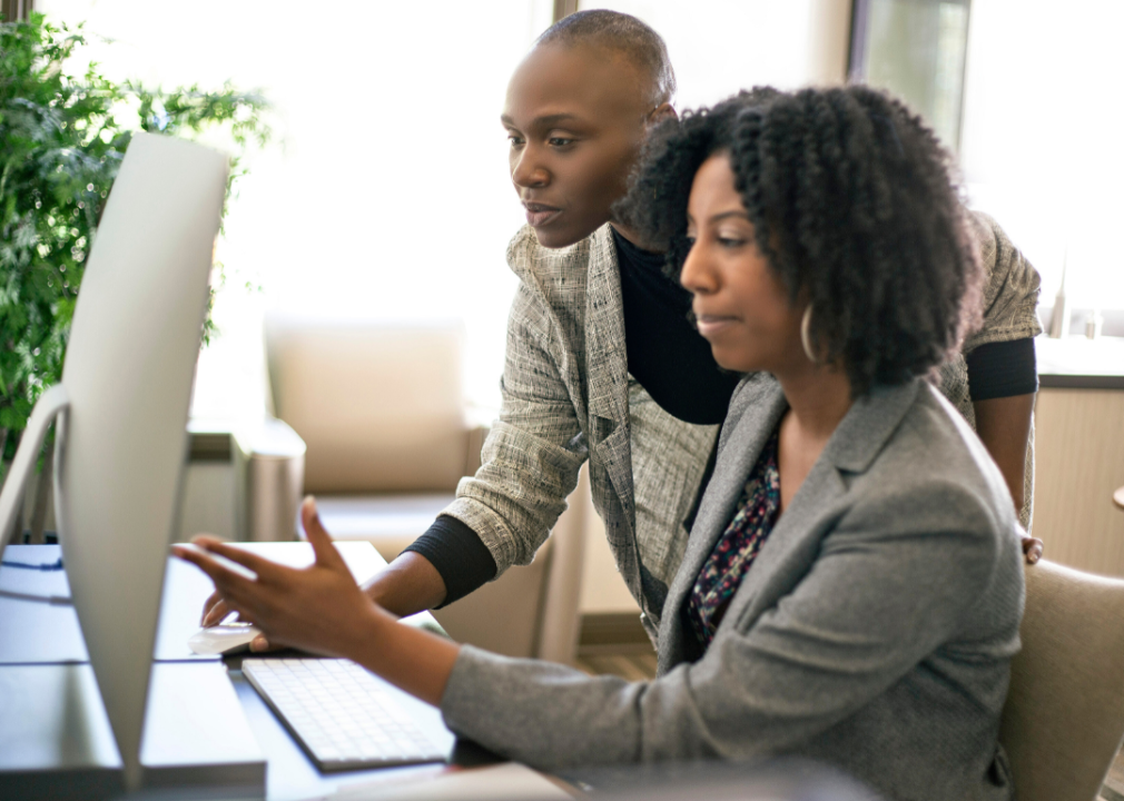 Two women discuss a document on their computer screen.