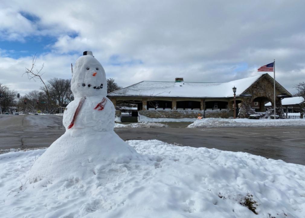 A snowman in front of a train station.