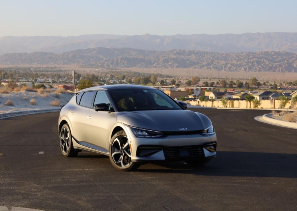 A silver Kia electric vehicle in a neighborhood with a desert and mountains in the background.