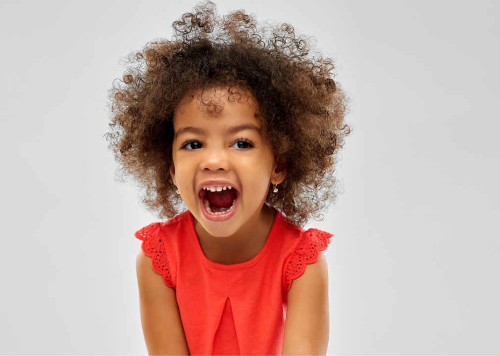 Child with curly brown hair and red t-shirt laughing.