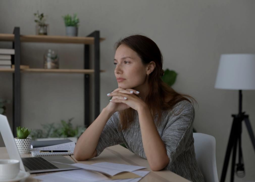 A woman sitting at a desk resting her chin on her hands with her fingers interlocked. She