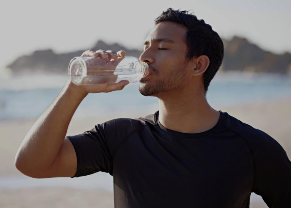 A young man tilting a water bottle to his mouth. 