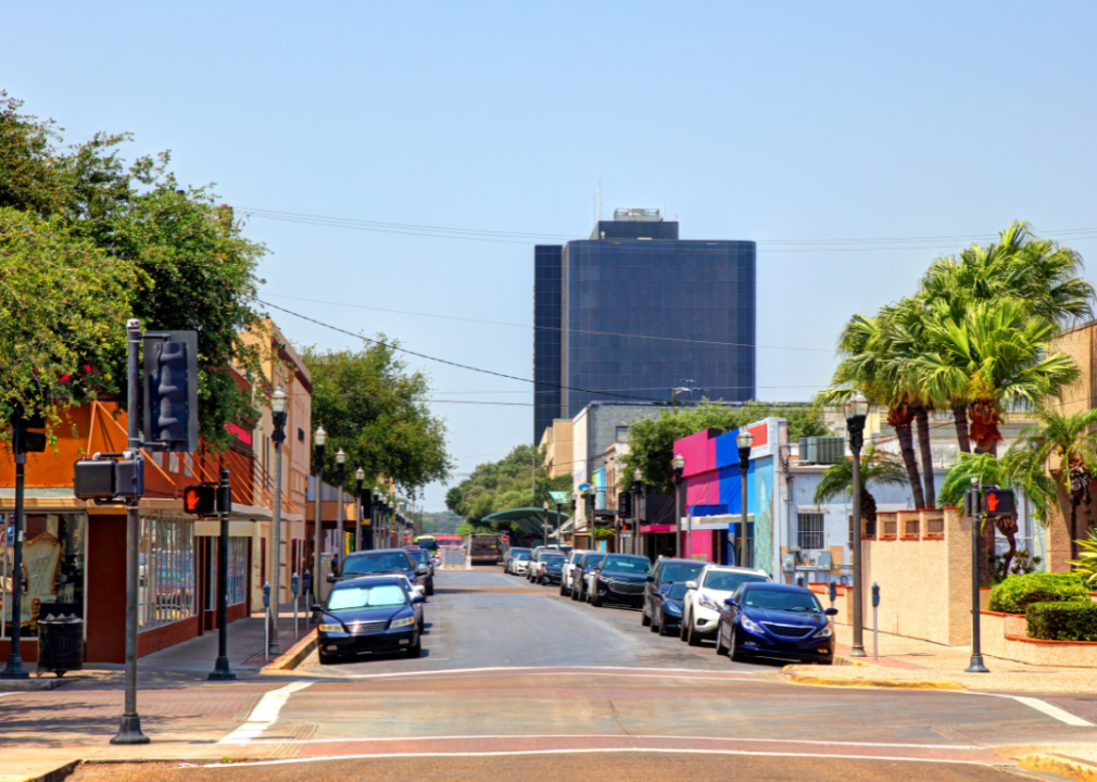 A row of cars parked on the side of a street, with a tall building in the background.