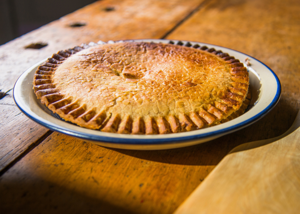 A whole pie with a flaky, golden crust on a white ceramic plate.