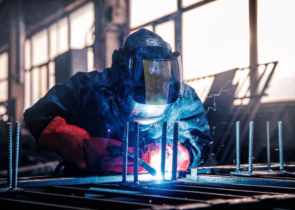 A welder in protective gear, including a mask, working on metal.