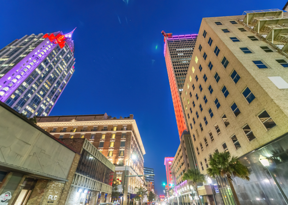 A city street of Mobile with tall buildings and palm trees at night. 