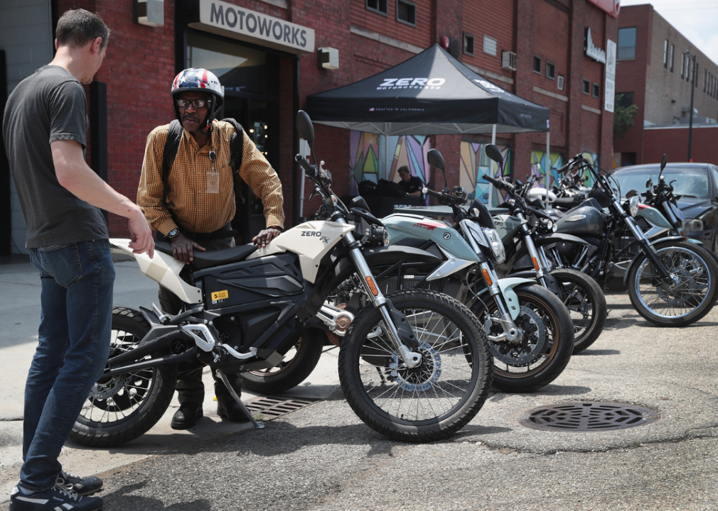 Two men look at electric motorcycles outside a bike shop.