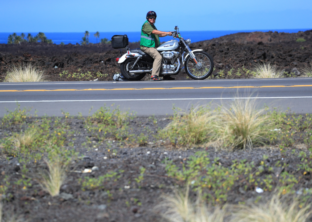 A man on a motorcycle on the highway with the ocean in the background.