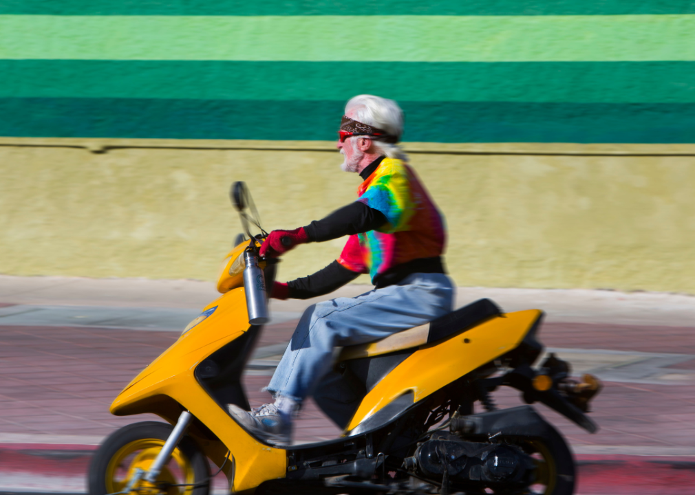 An elderly man in a tie-dye shirt riding a motorcycle in Las Vegas, NV.