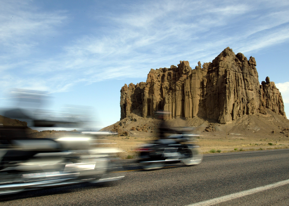Two motorcycles speed past a rock formation.