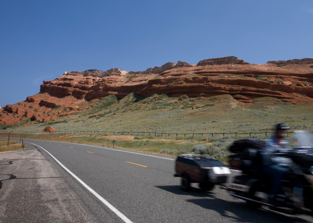 A motorcycle and trailer passing through a national park with rock formations in the background.