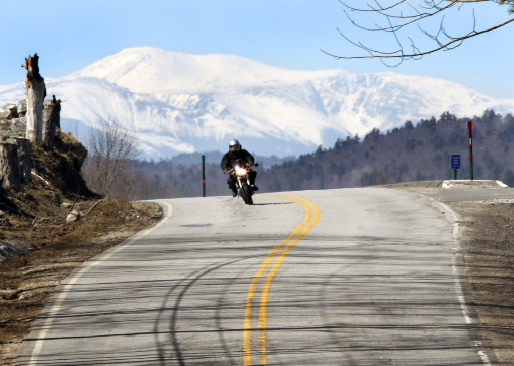A motorcyclist riding over a hill with Mount Washington in the background.