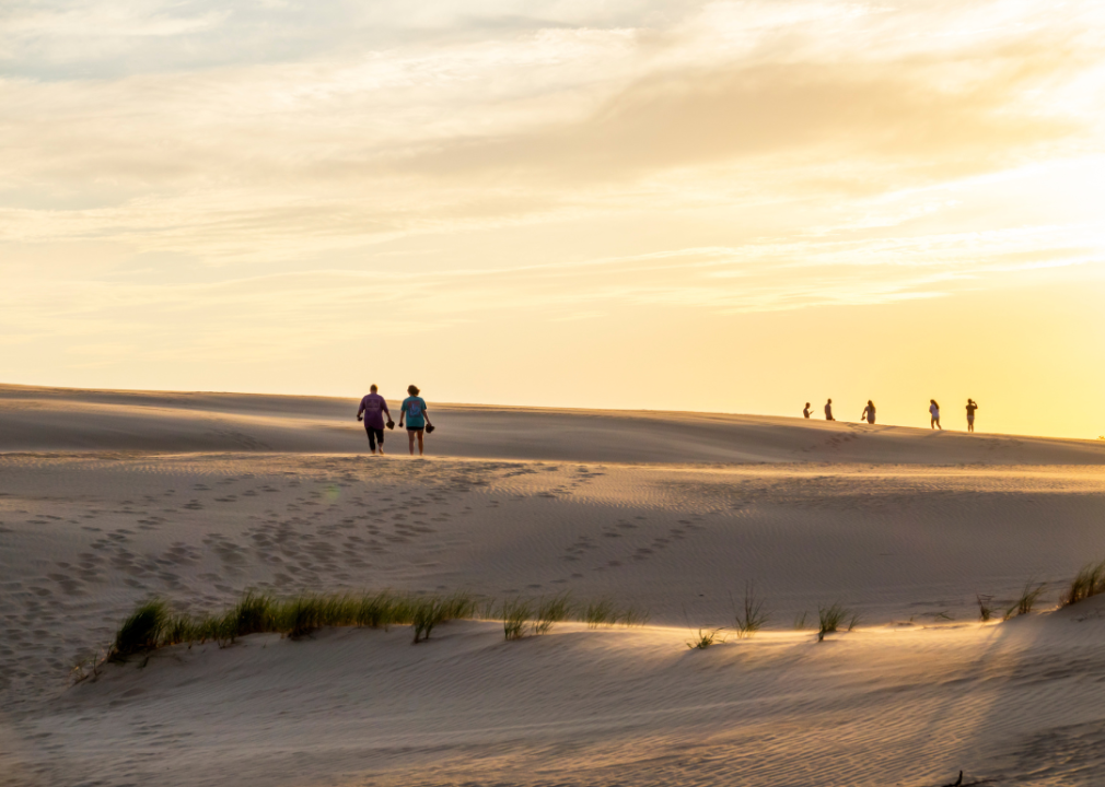 People walking on sand dunes at sunset.