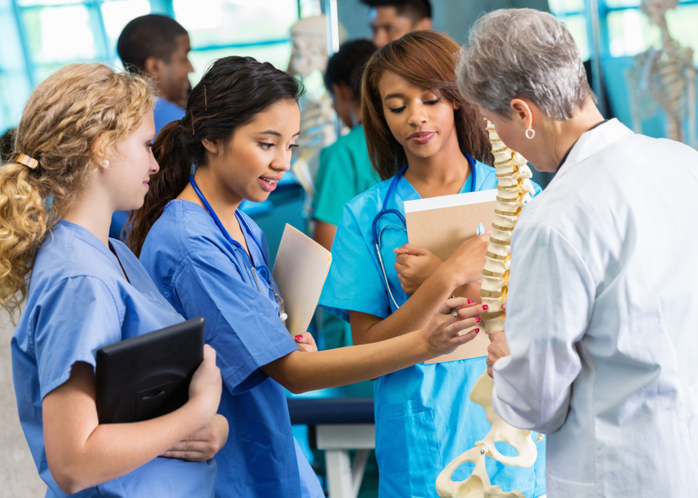 Three nursing students look at a model of a spine.