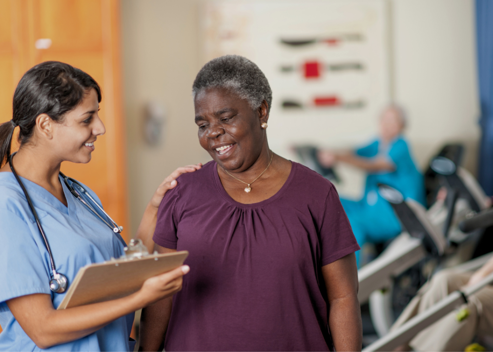 An older Black woman standing close to the nurse with a clipboard.