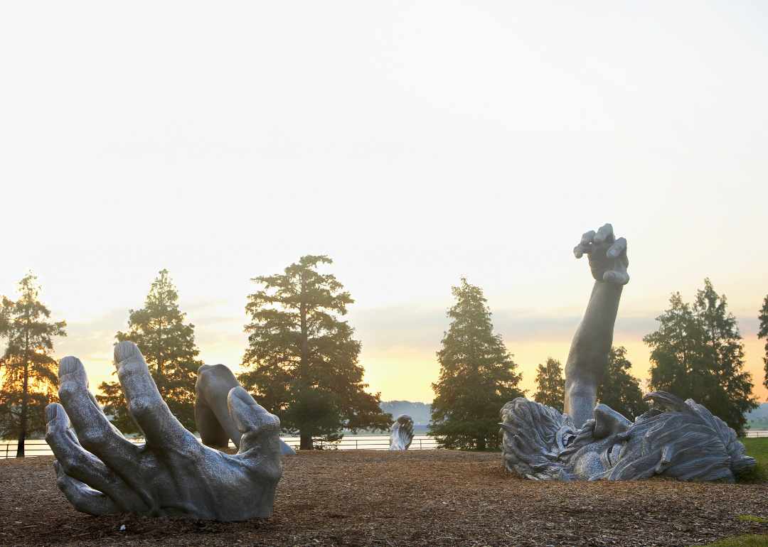 A park with a large sculpture of a man's head, arms and legs coming out of the ground.