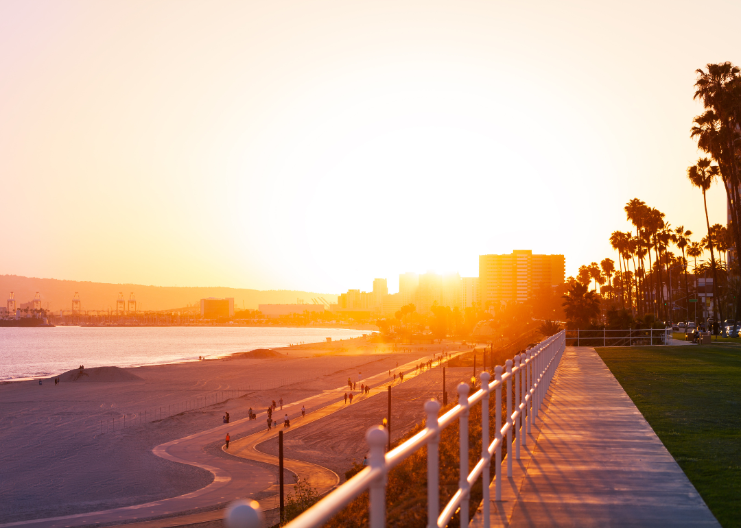 The boardwalk and people walking on the beach at sunset.