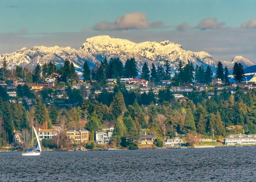 A sailboat on the water with large homes and mountains in the background.