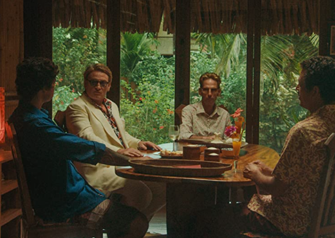 A scene from Pacification with four men sitting around a table.