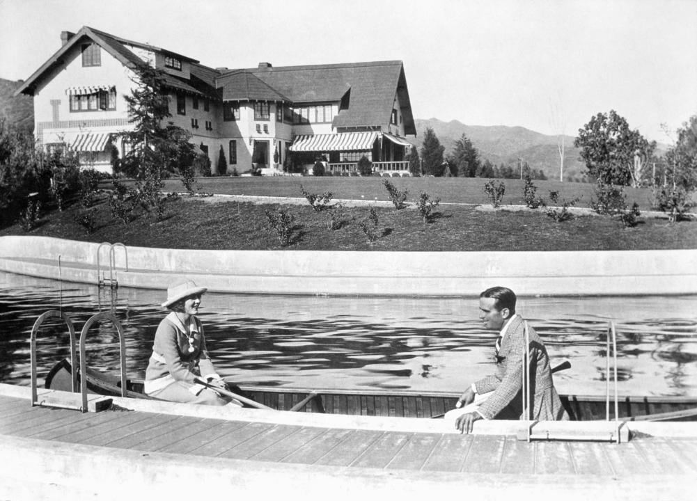 Douglas Fairbanks and Mary Pickford canoe along the swimming pool at their Pickfair estate.