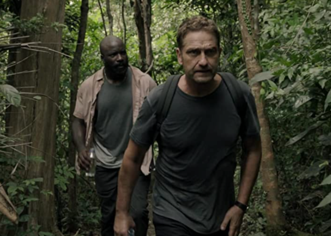 Gerard Butler and Mike Colter walking through a wooded area in Plane.