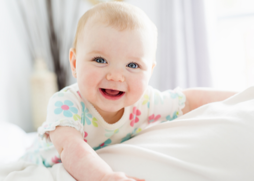 A baby girl in white bedding smiling.