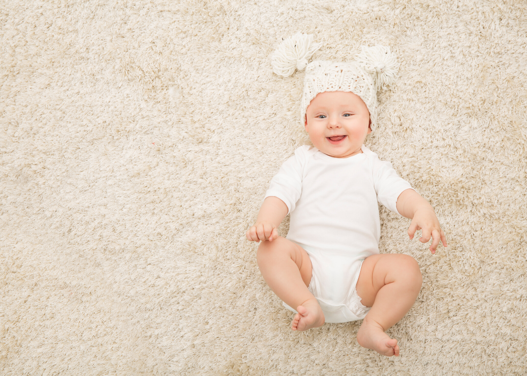 Happy baby in hat and diaper lying on carpet.